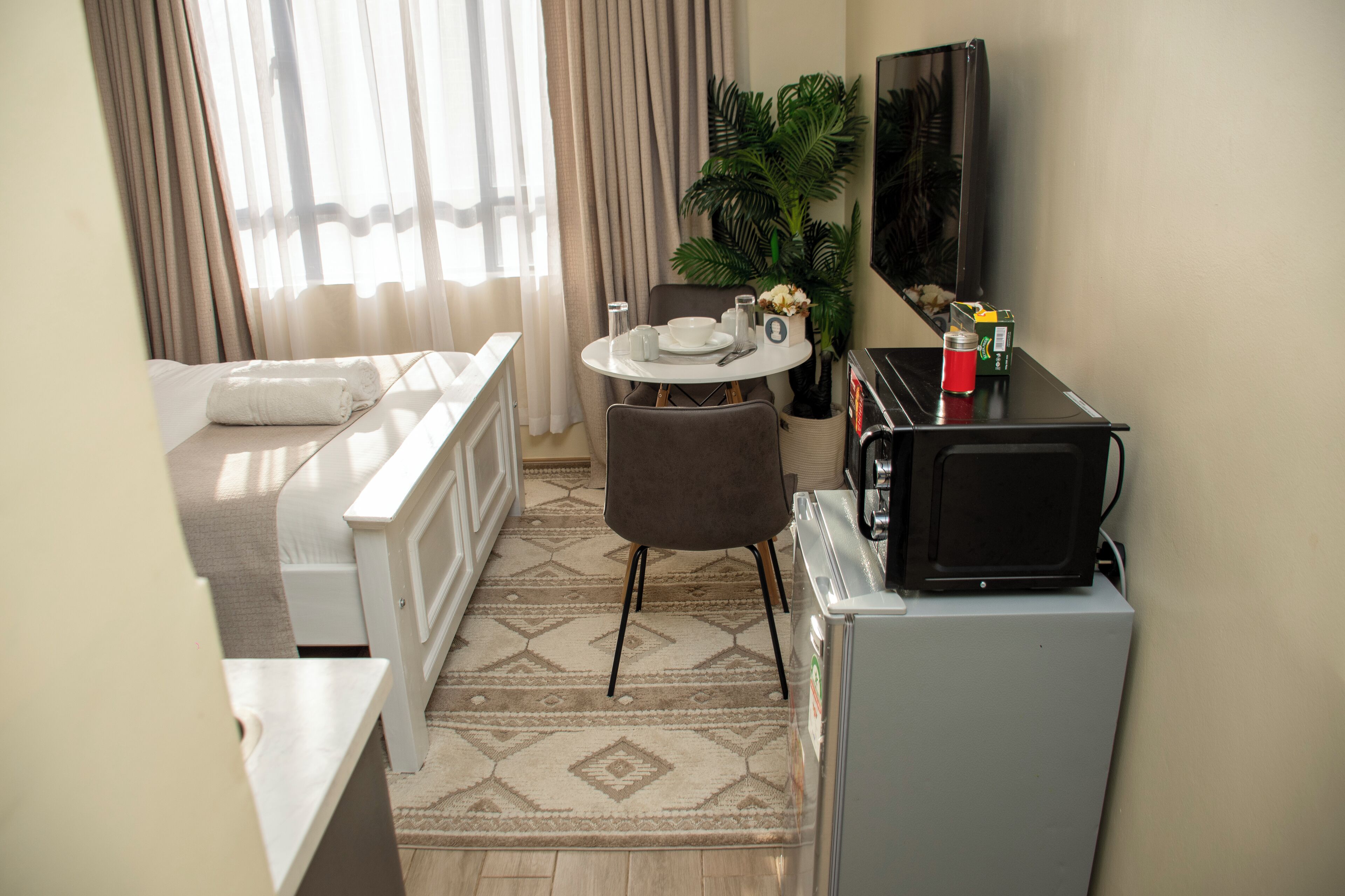 Habitación de hotel pequeña con cama, una mesa de comedor con sillas, microondas y refrigerador.