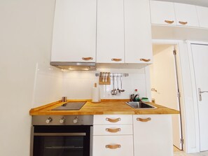 Une cuisine compacte avec des meubles blancs, un plan de travail en bois, un four encastré et un évier en acier inoxydable.