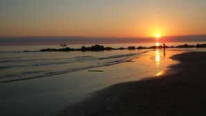 Ein Strand bei Sonnenuntergang mit klarem Himmel, ruhiger See und einigen Felsen in der Ferne.