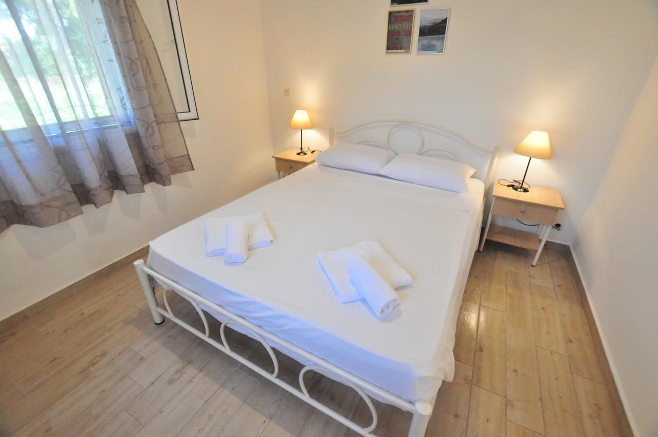 Una cama bien hecha con sábanas y toallas blancas, dos mesitas de noche con lámparas, una ventana con cortinas y un cartel en la pared.