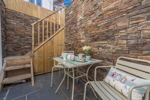 A patio with a stone wall, wooden staircase, and outdoor furniture including a table and chairs.