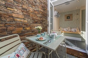 A dining area with a stone wall, a table with a placemat, a bench, and a window seat with cushions.