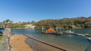 Una marina costera con una playa de arena, un muelle con barcos y casas al fondo.