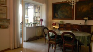 A dining area with a table set for four, surrounded by chairs, a chandelier, and a bookshelf in the background. - Large, elegant apartment on Janiculum hill, from 2 to 8 persons. (Roma)