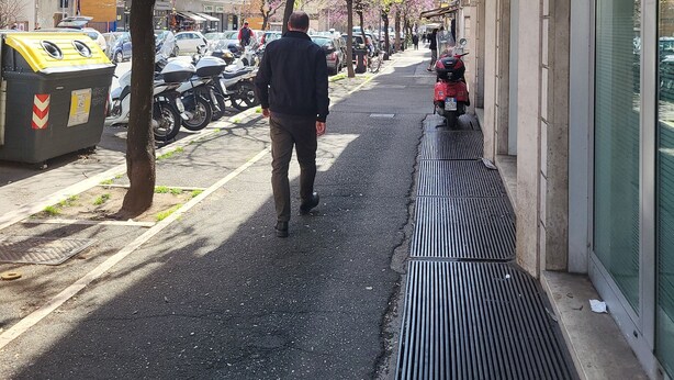 A man walking on a tree-lined sidewalk next to a building with a trash bin and parked motorcycles. - Large, elegant apartment on Janiculum hill, from 2 to 8 persons. (Roma)