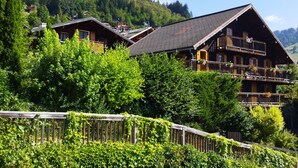 A chalet-style building with multiple balconies, surrounded by lush greenery and set against a mountainous backdrop.