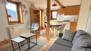 A cozy living room with a grey sofa, a wooden dining table, and a kitchen in the background.