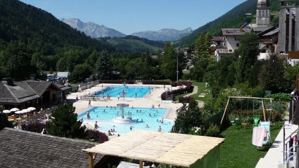 A swimming pool area with multiple pools, surrounded by lush greenery and mountains in the background.