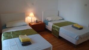 Habitación de hotel con dos camas individuales, cada una con una almohada, una mesita de noche con una lámpara y una manta verde en una de las camas.
