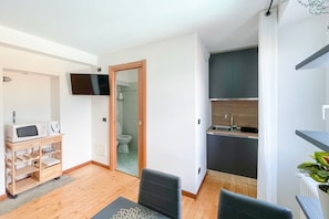 Een knus woongedeelte met een kitchenette, een aan de muur bevestigde televisie en een houten kast met apparatuur.