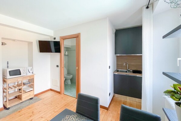 A compact living space with a kitchenette, a TV mounted on the wall, and a wooden cabinet with appliances.