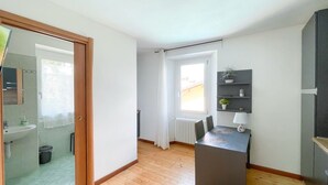 Eine moderne Wohnung mit Holzboden, einer Küchenzeile inklusive Einbaukühlschrank, einem kleinen Esstisch und einem Fenster mit Vorhängen.