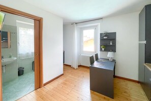 Un appartement moderne doté d’un plancher en bois, d’un coin cuisine avec un réfrigérateur intégré, d’une petite table à manger et d’une fenêtre avec des rideaux.