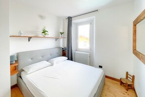 Ein Schlafzimmer mit einem großen Bett, einem Holzkopfende, Nachttischen, einem Heizkörper, einem Fenster mit Blick und einem kleinen Holzstuhl.
