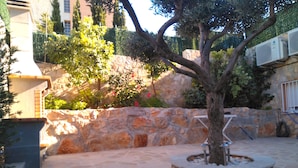 Ein steinerner Innenhof mit einem Baum in der Mitte, umgeben von einer Steinmauer und einem Gebäude mit Klimaanlagen.