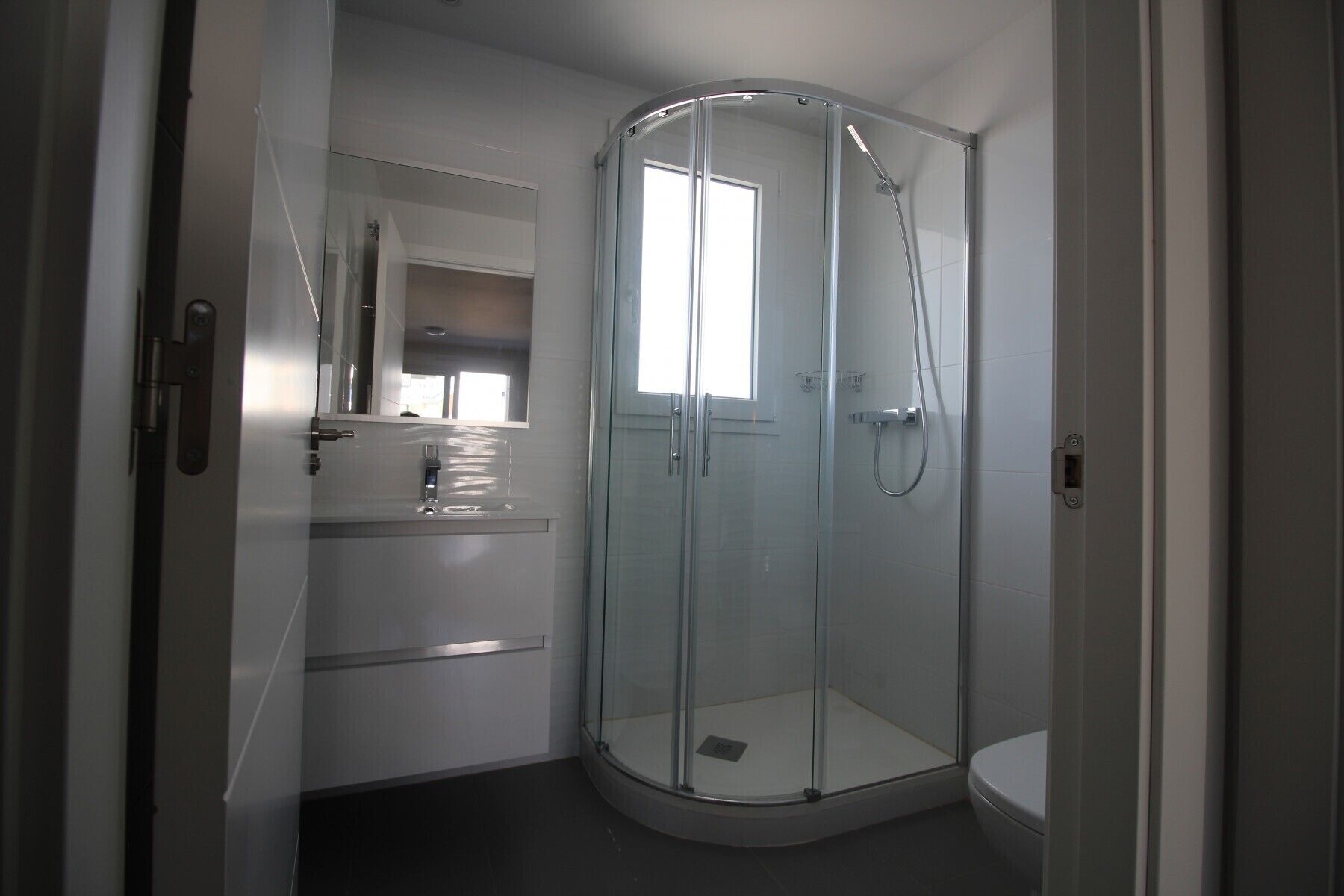 A modern bathroom with a glass-enclosed shower, a toilet, and a sink with a mirror above it.