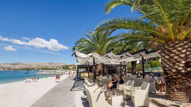 Ein Café am Strand mit Außenbestuhlung, Palmen und Meerblick.