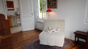 Una habitación con piso de madera, una silla blanca con cojín floral, una lámpara roja y un cuadro en la pared.