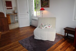 Ein Zimmer mit Holzboden, einem weißen Stuhl mit floraler Sitzkissen, einer roten Stehlampe und einem Bild an der Wand.