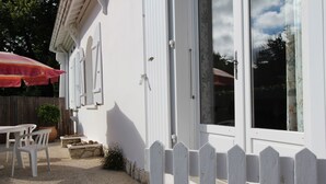 Una casa blanca con valla de piquete blanca, un patio con mesa y sillas, y una sombrilla grande.