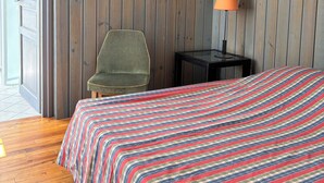 Una habitación con una cama, una silla, una lámpara y un muro de madera.