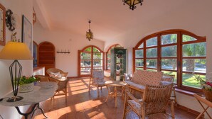 A sunlit room with wicker furniture, large windows, and a decorative lamp. - Villa in dream location with private pool right by the sea (Siracusa)