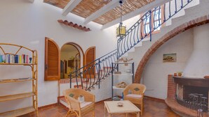 A cozy room with a tiled floor, wicker furniture, a bookshelf, a staircase, and a fireplace. - Villa in dream location with private pool right by the sea (Siracusa)