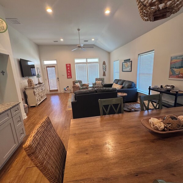 A spacious living area with a wooden dining table, a sofa, and a television mounted on the wall.