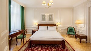 Habitació d'hotel amb un llit gran, una taula de treball, una cadira, una làmpada i un penjallum.
