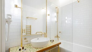 Un bany modern amb un lavabo blanc, detalls daurats i una dutxa amb envàs de vidre.