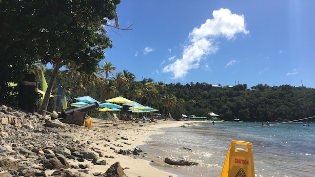 A beach with umbrellas, a caution sign, and rocky terrain. - Come sail the Caribbean Sea aboard Antillean  (St thomas)