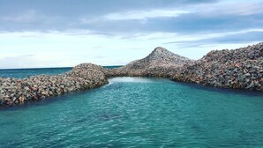 A clear view of a coastal area with a rocky breakwater extending into turquoise waters. - Come sail the Caribbean Sea aboard Antillean  (St thomas)
