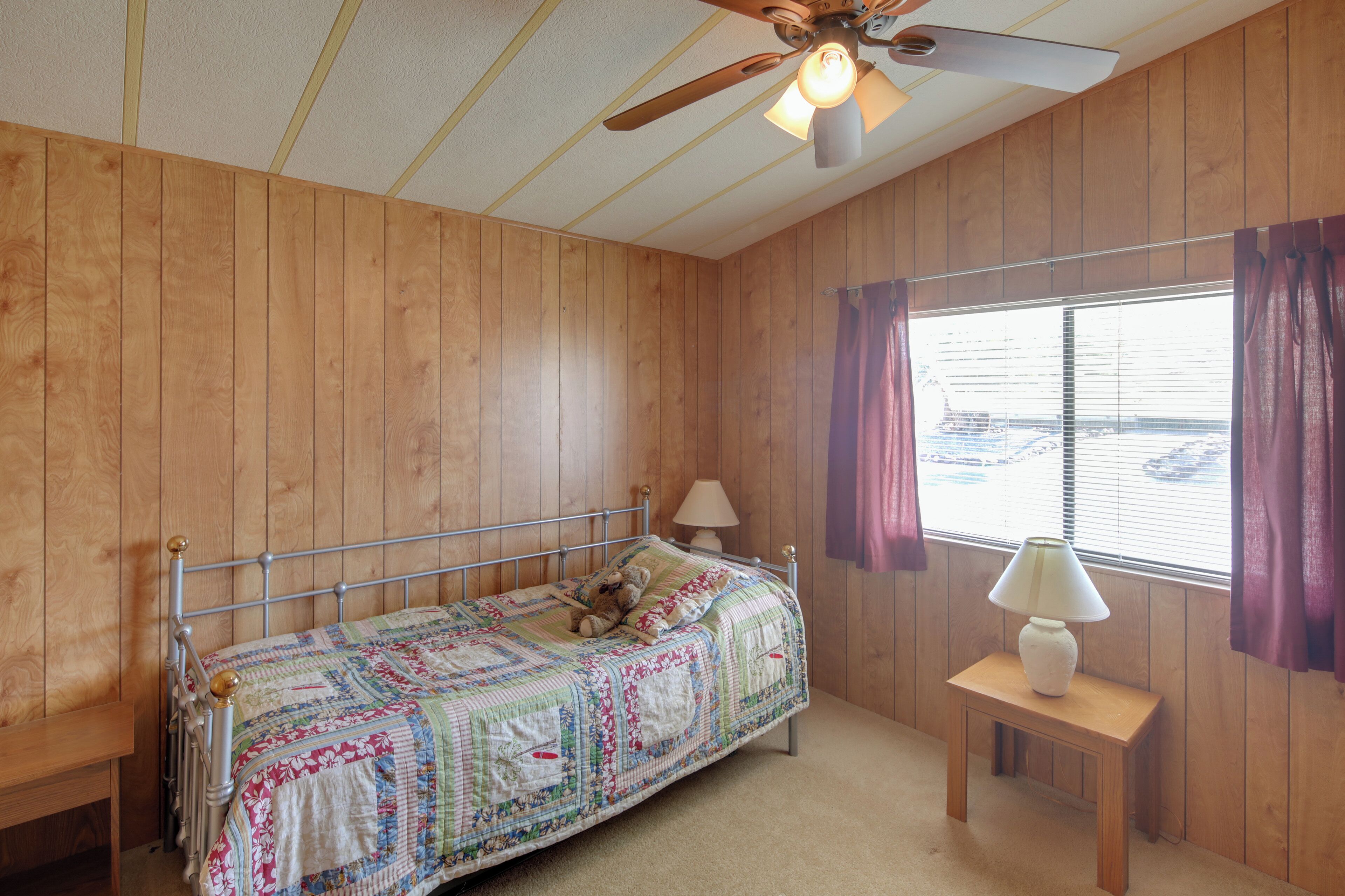 A bedroom with a wooden paneled wall, a metal bed frame, a bedside table with a lamp, and a window with curtains.
