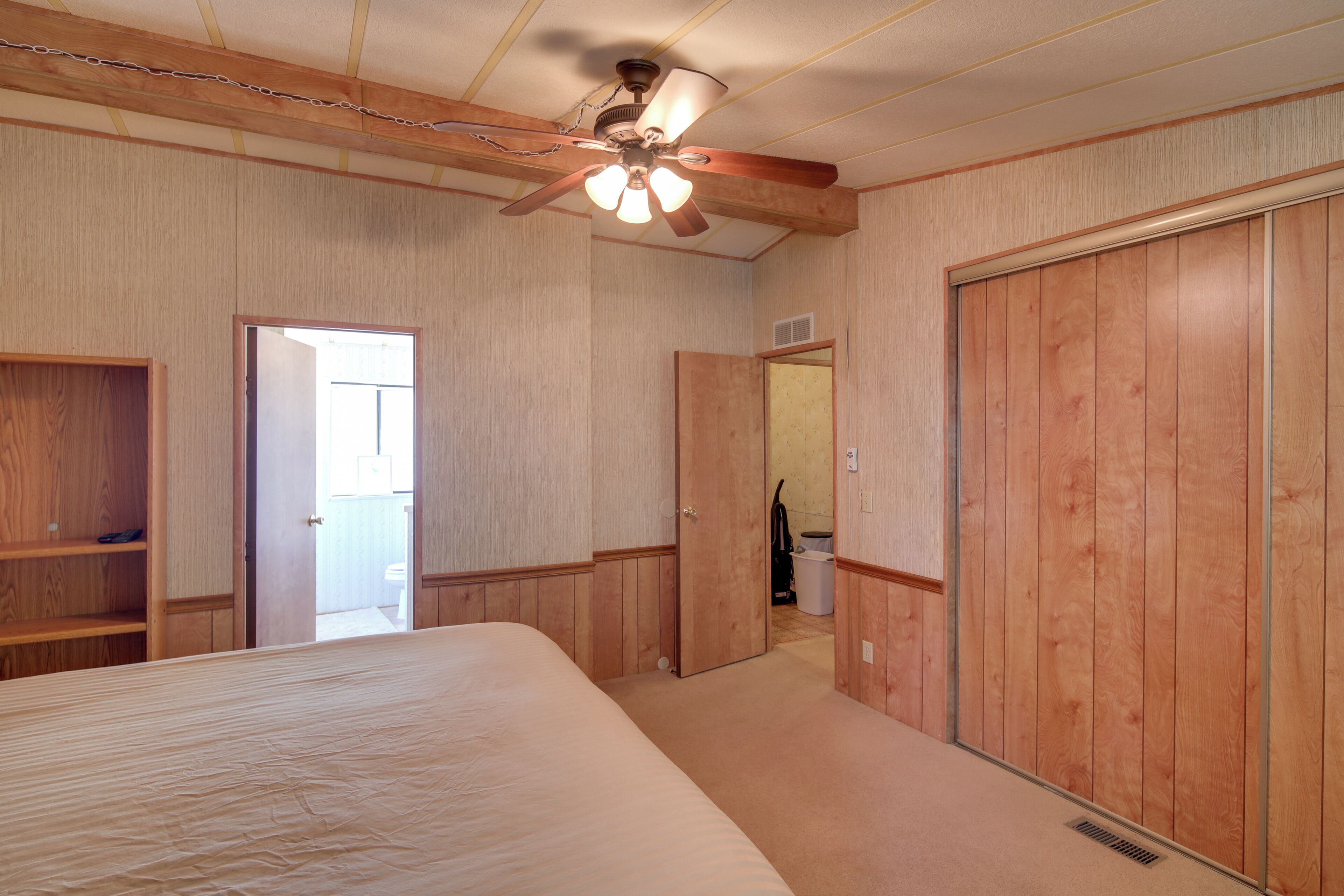 A bedroom with a wooden wardrobe, a ceiling fan, and a door leading to another room.