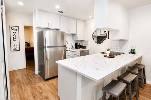 A modern kitchen with white cabinets, a stainless steel refrigerator, a marble countertop, and a bar stool area.