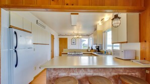 A kitchen with wooden cabinets, a white refrigerator, a microwave, and a large island with stools. - Rustic Coastal Smith River Cottage w/ Ocean Views! (Smith River)