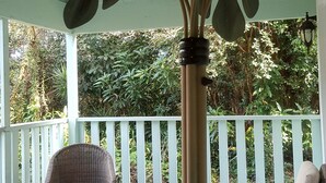 Un área de estar al aire libre techada con mobiliario de mimbre y una planta artificial grande.