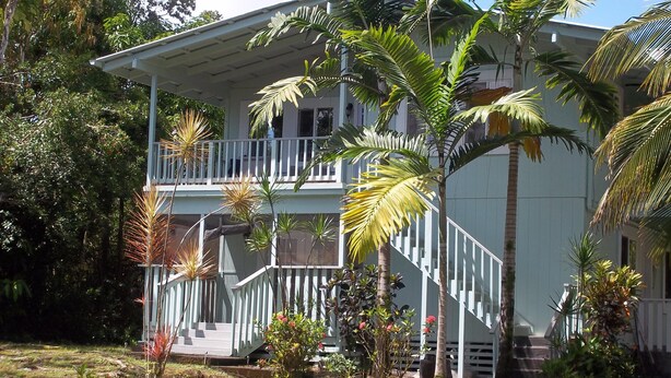 Una casa de dos pisos con balcón, rodeada de vegetación tropical.