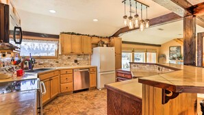 A kitchen with wooden cabinets, a stainless steel dishwasher, a white refrigerator, and a wooden bar counter. - South Dakota Vacation Rental Near Mount Rushmore (Hermosa)