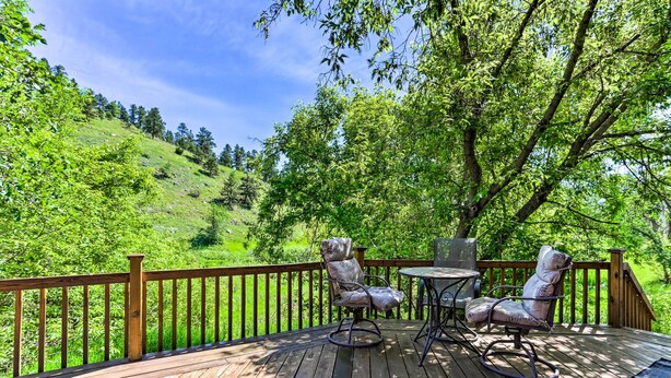 A wooden deck with two rocking chairs and a small table, overlooking a lush green hillside. - South Dakota Vacation Rental Near Mount Rushmore (Hermosa)