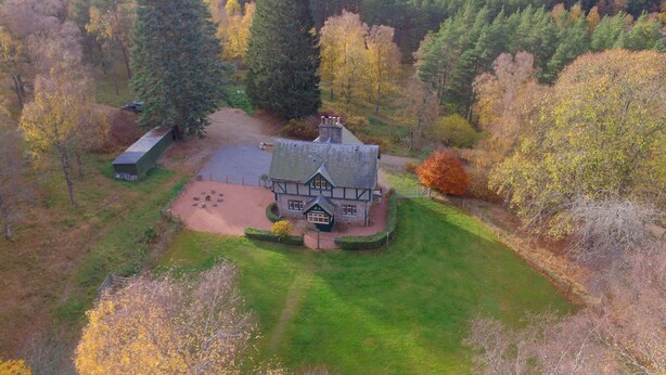 Luchtbeeld van een huis, omringd door bos, met een verzorgd gazon en een grindpad.