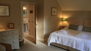 Een slaapkamer met een groot bed, een dressoir, een nachtkastje en een deur naar een badkamer.