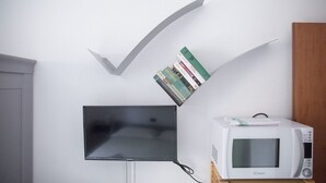 Un televisor de pantalla plana montado en la pared, una pila de libros apoyados contra la pared y un microondas sobre un soporte de madera.