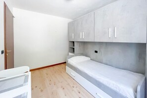 Een slaapkamer met een eenpersoonsbed, grijze kastjes en een houten vloer.