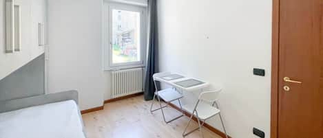 A small, bright room with a bed, a window with a view, a table with chairs, and a door.