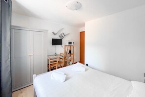 A bedroom with a bed, a desk, a chair, a TV, and a wardrobe.