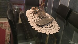 A dining table with a glass top, surrounded by black leather chairs, a lace table runner, and a vase with flowers. - High standing apartment in Guéliz 2 minutes from Carre Eden (Marrakech)