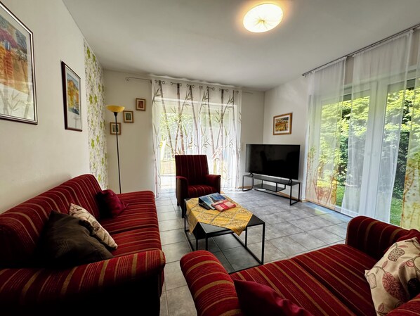 Ein Wohnzimmer mit einer Sofagarnitur, einem Fernseher und einem Tisch mit Büchern.