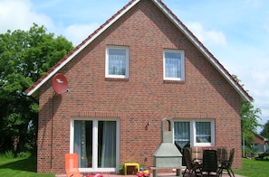 Une maison à deux étages, construite en briques, avec une cheminée, une terrasse dotée de mobilier d’extérieur et une antenne parabolique.