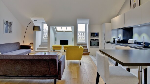 A modern living space with a sofa, yellow chairs, a dining table, and a kitchen area with appliances.